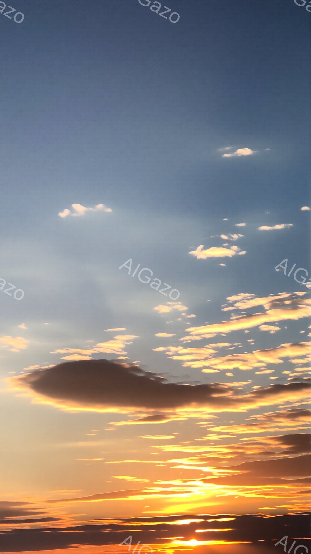 空は夕焼けに染まり、オレンジ、黄色、そしてわずかな赤色のグラデーションが広がっている。雲はまるで燃えているかのように輝き、空全体にドラマチックな模様を描いている。下の方には太陽が薄っすらと見え隠れし、 - AI生成フリー素材