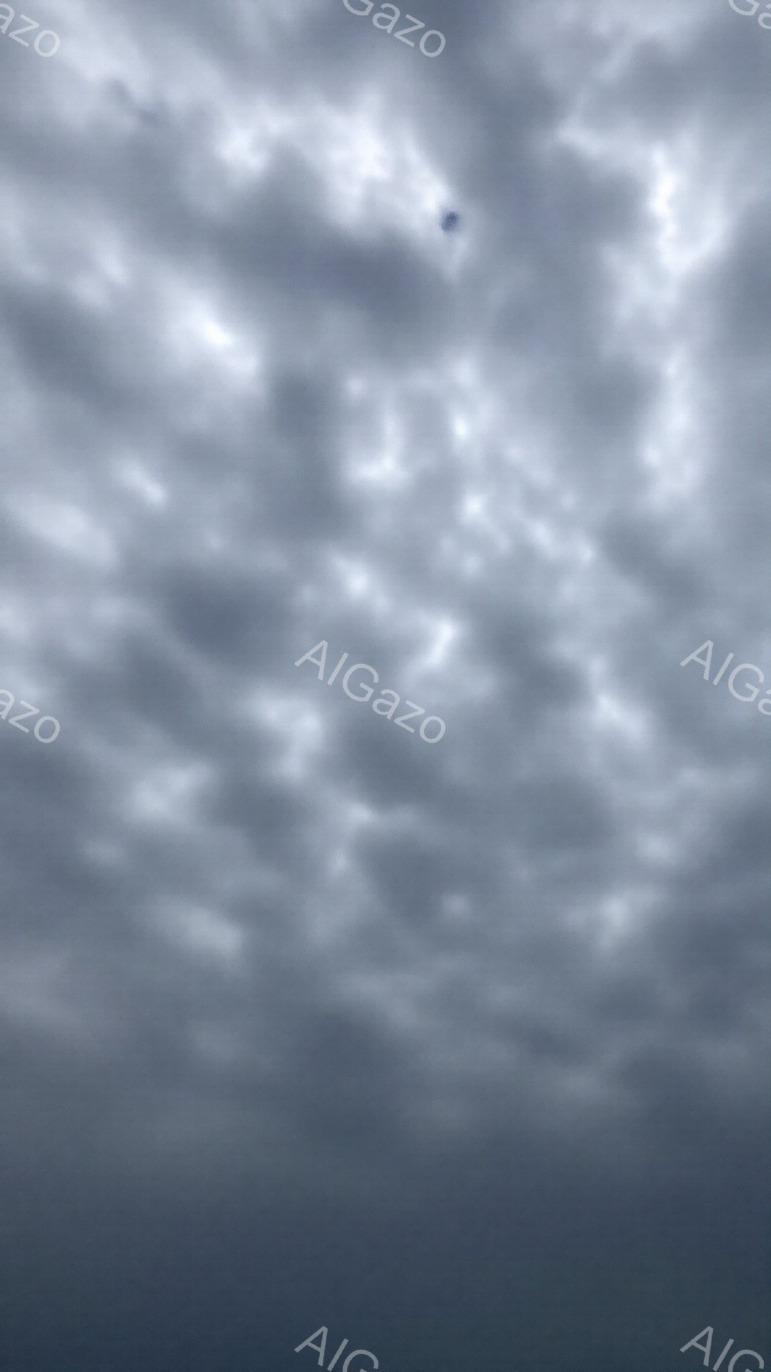 灰色がかった空が広がっており、厚い雲が覆い尽くしている。雲は層状で、暗い影と明るい部分が混ざり合い、重苦しい雰囲気を作り出している。ごくわずかに、雲の中に小さな飛行機が確認できる。 - AI生成フリー素材