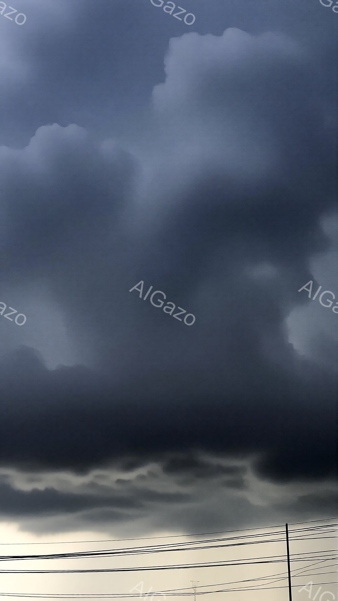 濃い灰色の雲が空を覆い、重々しい雰囲気を醸し出しています。下部には、薄い雲が水平に広がり、まるで海のような印象を与えます。電線が画面下部に走り、天候の厳しさを際立たせています。