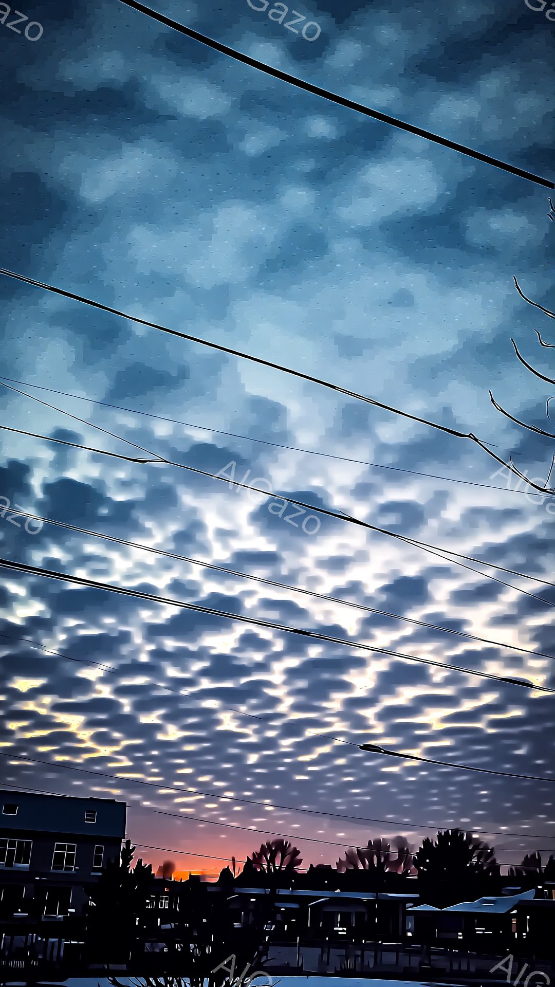雲海のような細かい雲が空一面に広がり、夕焼けの光を受けて金色やオレンジ色に輝いている。地平線にはシルエットになった建物や木々が見え、電線が画面上部を横切っている。空と建物のコントラストが印象的で、静寂と幻想的な雰囲気が漂う。
