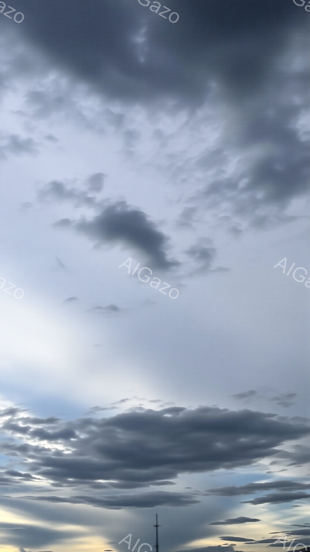 空は厚い雲に覆われ、一部に光が差し込み、ドラマチックなコントラストを生み出しています。雲は灰色と白のさまざまな色合いを持ち、遠くには塔のような構造物がわずかに見えます。全体的に、嵐の前や後の、重厚で静寂な雰囲気を感じさせます。