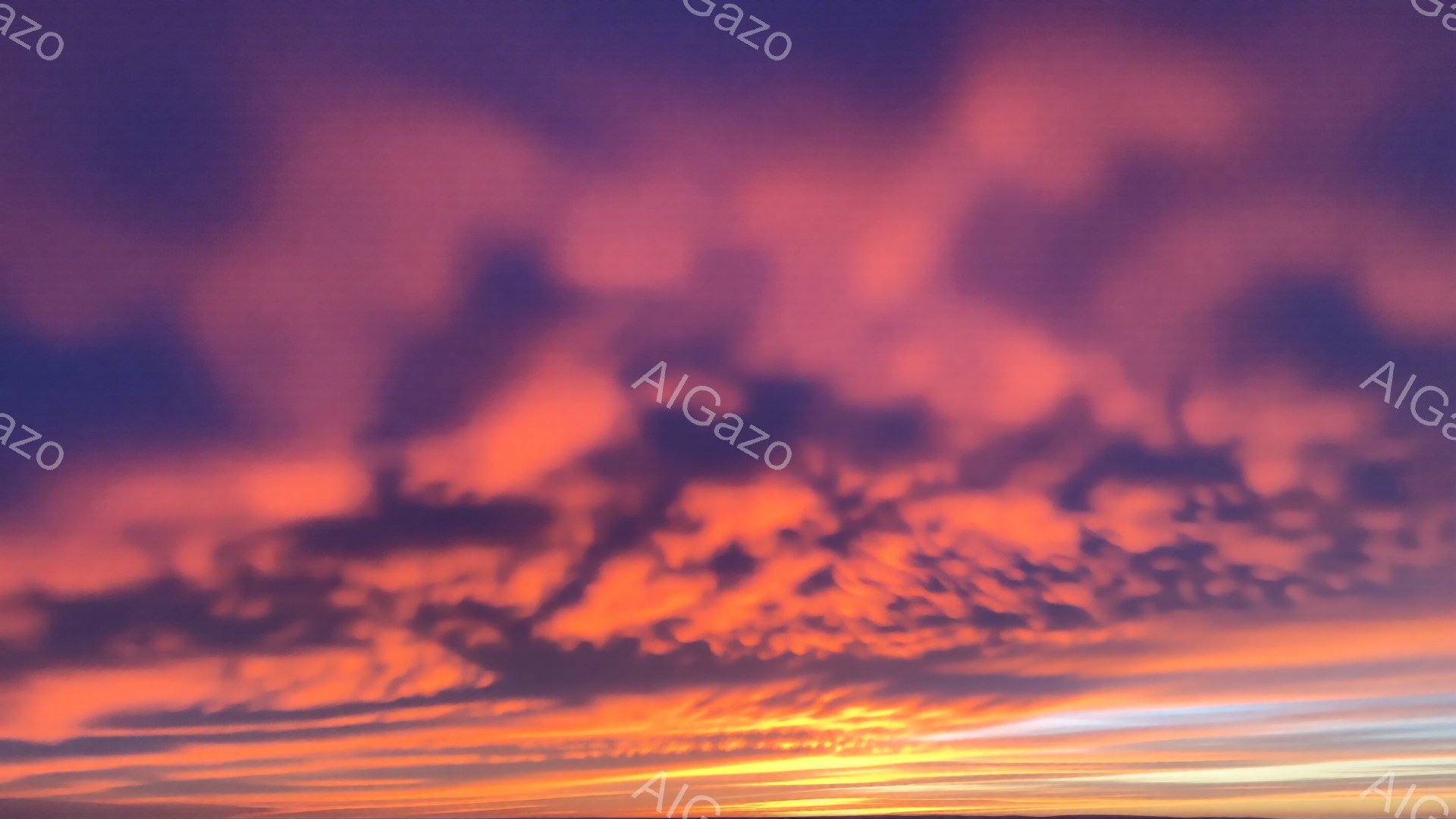 空は燃えるようなオレンジ色と鮮やかなピンク色の雲で覆われています。地平線近くには、太陽の光がほのかに輝き、雲に金色の縁取りを加えています。全体的に、力強く、鮮やかで、ドラマチックな夕焼けの雰囲気を感じさせます。