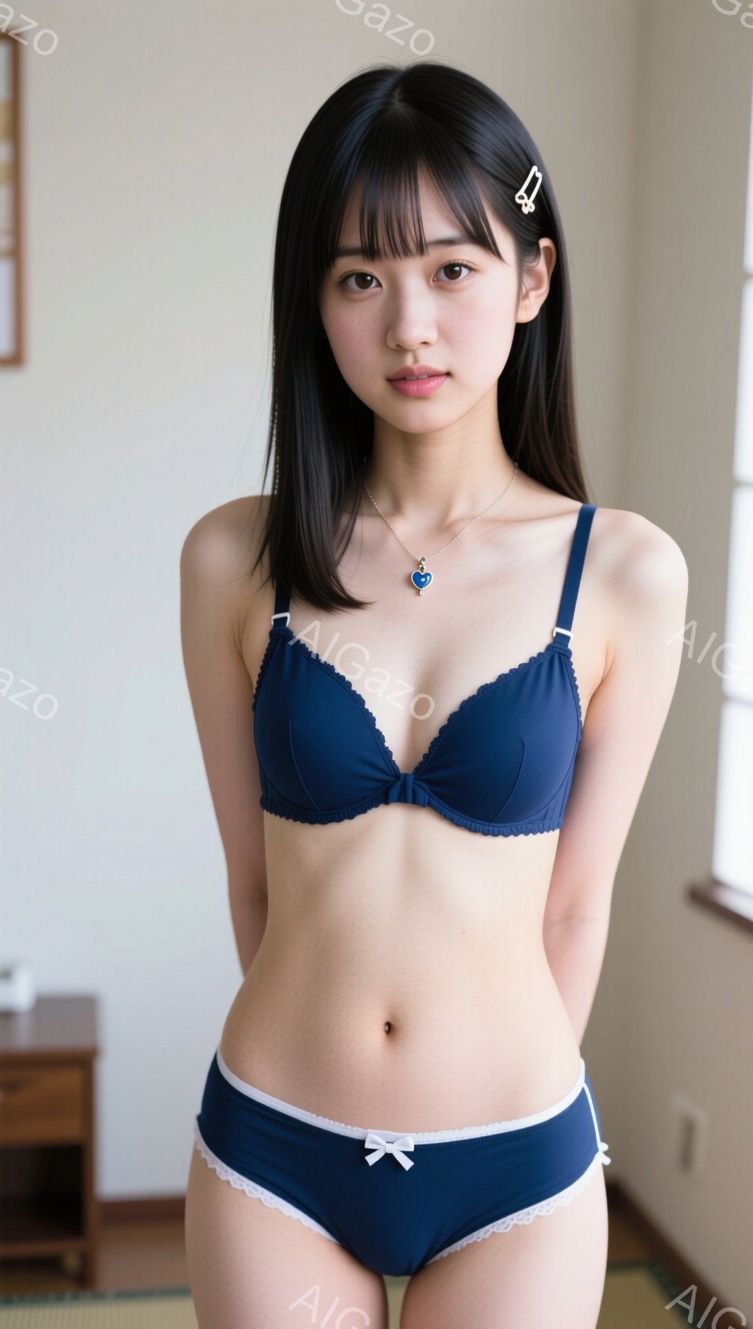 深い青色のブラとショーツを着用した若い女性が写っています。彼女は黒髪で、前髪は少しカールしており、サイドに白いヘアピンをつけています。背景はシンプルな室内で、窓から自然光が入っています。