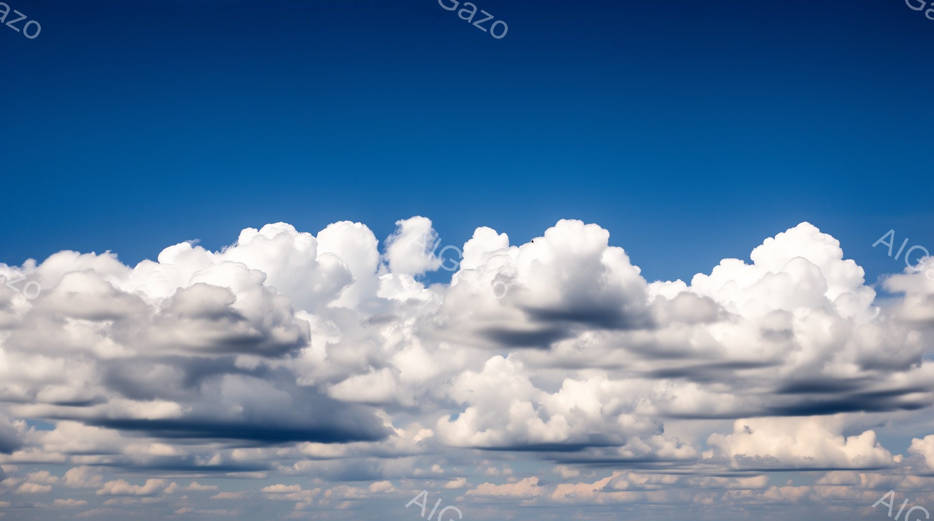 鮮やかな青空を背景に、白いふわふわとした雲が広範囲に広がっています。雲は塊状で、太陽光を浴びて明るく輝き、影の部分では灰色や薄い紫の色合いが見られます。全体的に穏やかで、平和な夏の日の雰囲気が漂います。