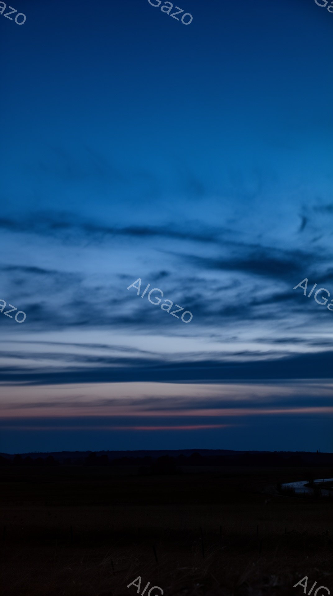 深い藍色の空が、地平線に向かって赤やオレンジのグラデーションに変化している。地平線付近には、暗いシルエットで草地や低い建物が確認でき、遠くの風景がシルエットで表現されている。全体的に静寂で神秘的な雰囲気で、夕暮れまたは夜明けの穏やかな時間帯を切り取った写真である。