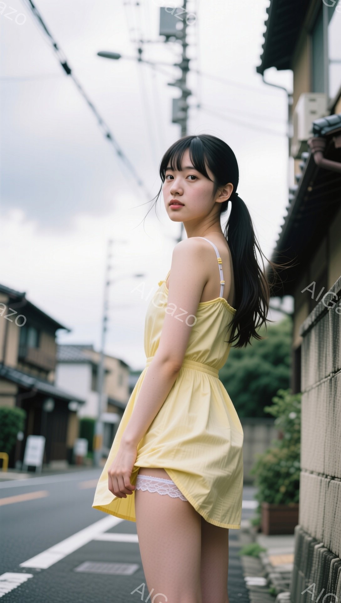 黒髪をポニーテールにした若い女性が、黄色いサスペンダーワンピースを着て、道路脇に立っている。彼女は少し振り返り、微笑みを浮かべており、白いレースのアンダースカートがワンピースの下から覗いている。背景には古い町並みが広がり、曇天の下、ノスタルジックな雰囲気が漂っている。