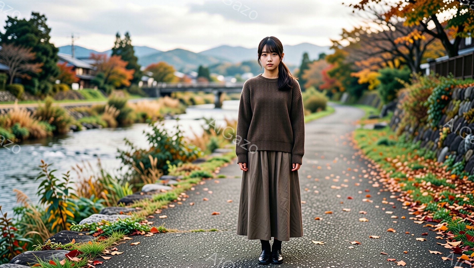 画像には、茶色のセーターとスカートを着た若い女性が写っています。彼女は正面をまっすぐ見ており、表情は穏やかで少し物憂げです。背景には、穏やかな川と、秋の紅葉が美しい自然豊かな風景が広がっており、全体的 - AI生成フリー素材