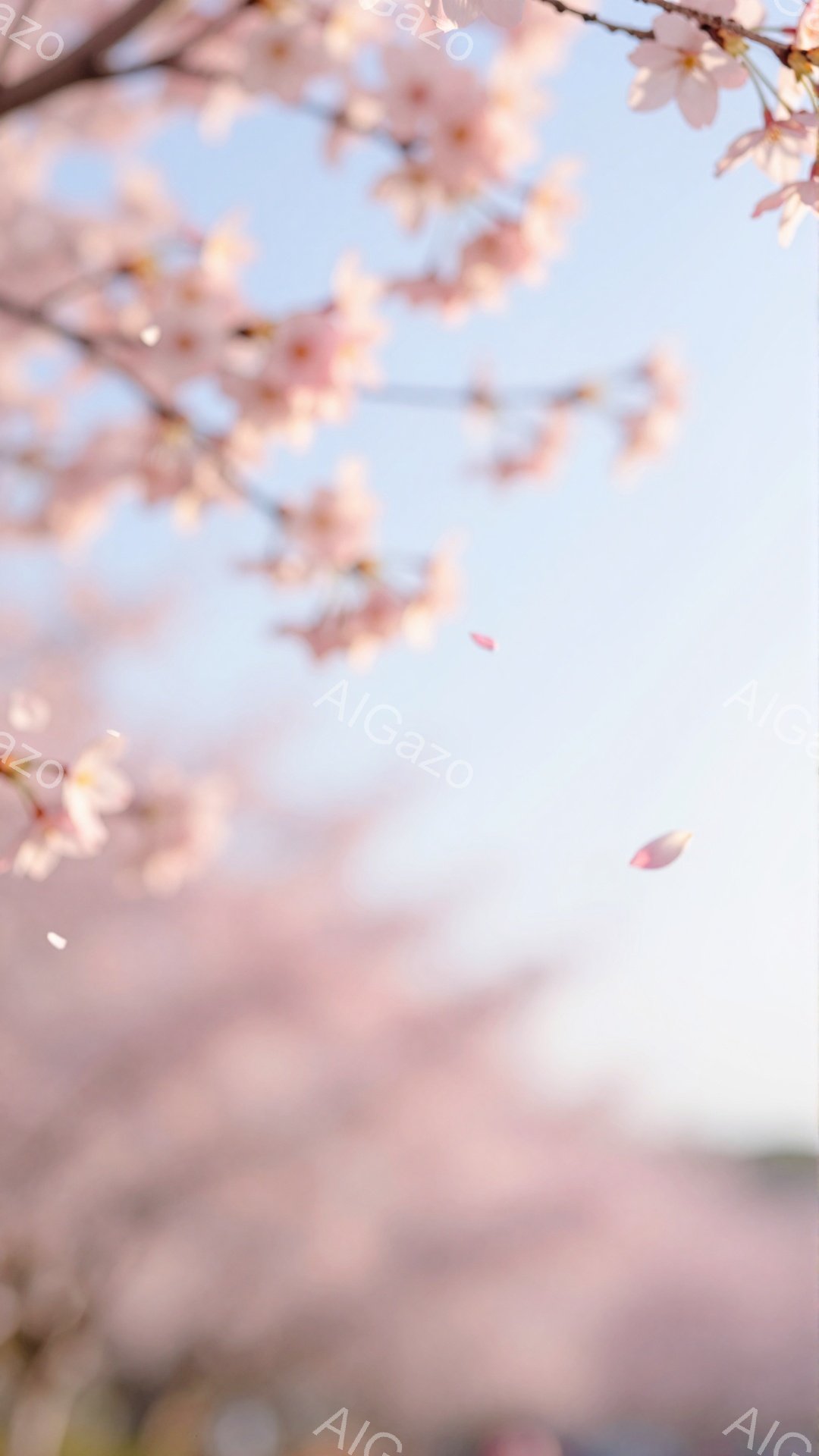 桜の花びらが舞い散る春の風景です。ぼやけた背景には、ピンク色の桜並木が広がり、柔らかい光が差し込んでいます。全体的に淡い色彩で、穏やかで幻想的な雰囲気を醸し出しています。