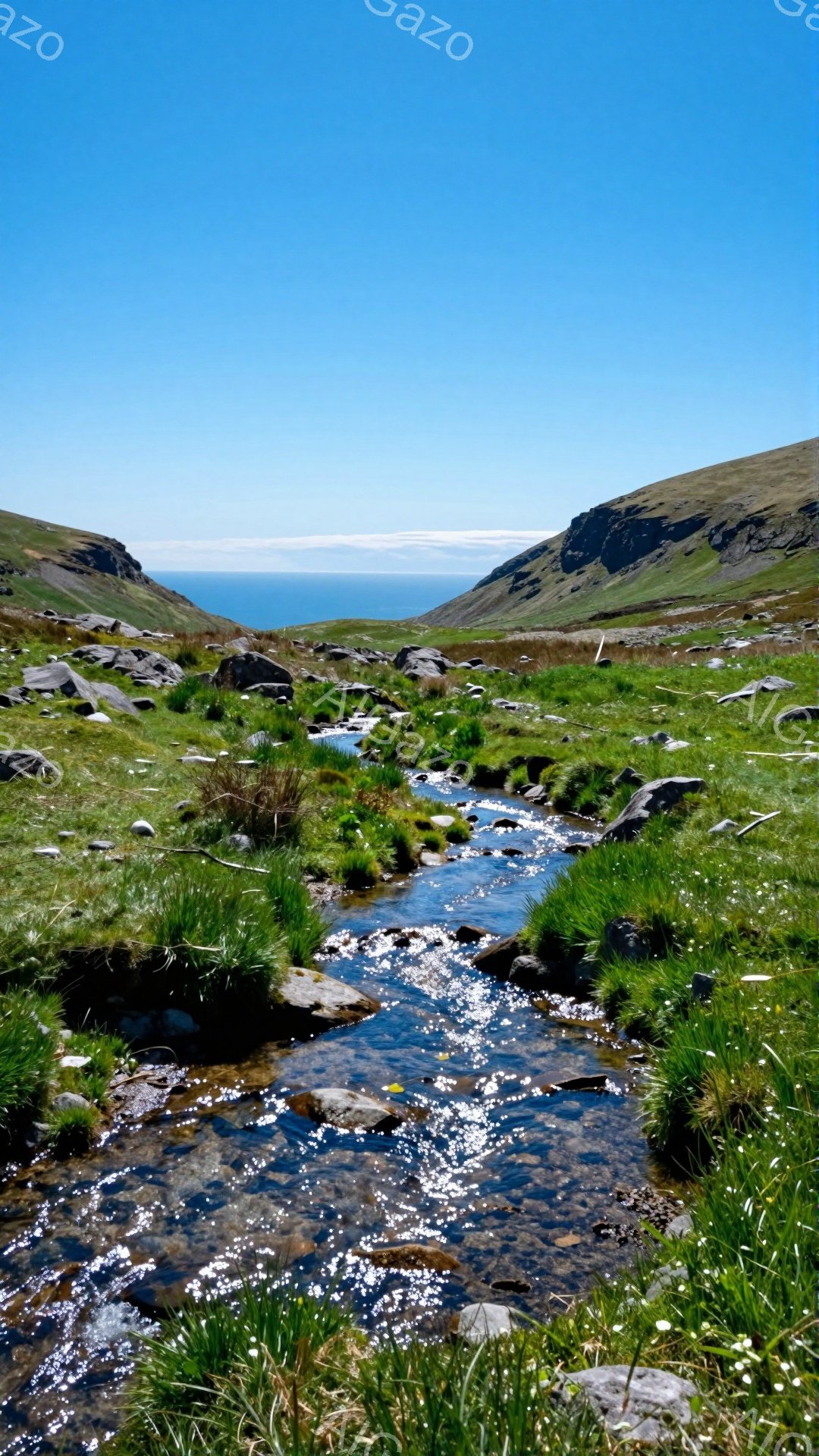 穏やかな流れが谷間を縫う風景です。緑の草と白い花が咲き乱れ、澄んだ水面が太陽の光を反射しています。背景には青い海と山々が広がり、静寂で美しい自然の姿が印象的です。